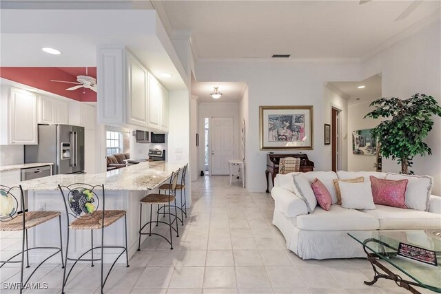 living room featuring white cabinetry, crown molding, a breakfast bar, and light stone counters