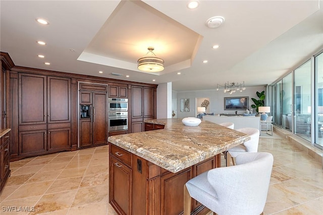 kitchen with light stone countertops, a large island, a raised ceiling, and a kitchen bar