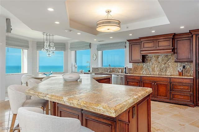 kitchen featuring dishwasher, a center island, a raised ceiling, pendant lighting, and a breakfast bar