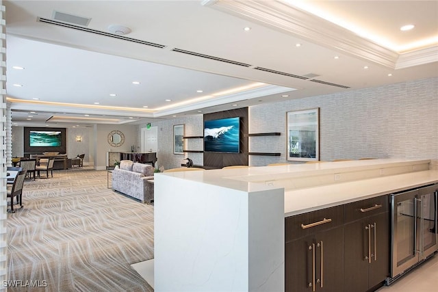 kitchen with a tray ceiling, light carpet, dark brown cabinets, and beverage cooler