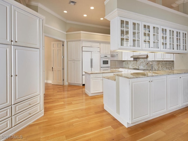 kitchen with built in appliances, white cabinets, light stone counters, and kitchen peninsula