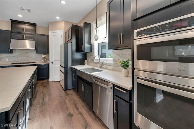 kitchen featuring sink, stainless steel appliances, hanging light fixtures, dark hardwood / wood-style flooring, and backsplash