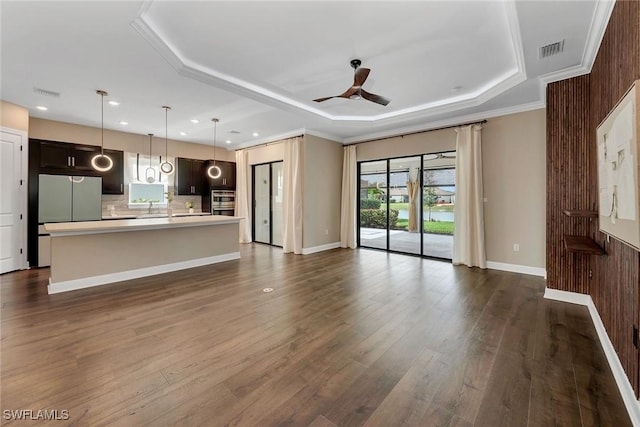 unfurnished living room with a tray ceiling, ceiling fan, crown molding, and dark hardwood / wood-style floors