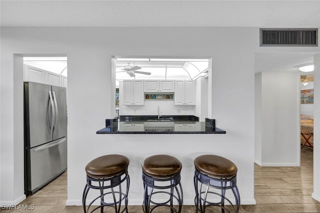 kitchen featuring white cabinets, stainless steel fridge, a kitchen bar, and kitchen peninsula