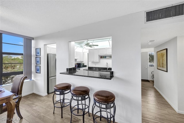 kitchen featuring white cabinets, sink, a textured ceiling, kitchen peninsula, and stainless steel refrigerator