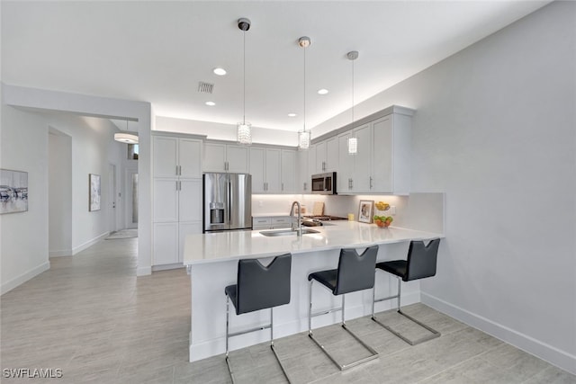 kitchen featuring sink, stainless steel appliances, kitchen peninsula, pendant lighting, and a breakfast bar area