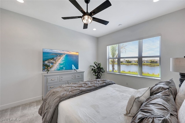 bedroom with ceiling fan, a water view, and light carpet