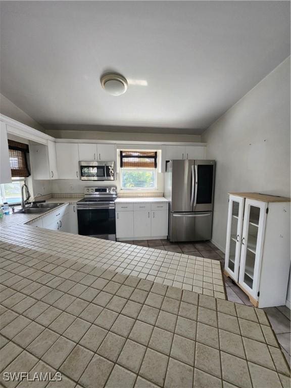 kitchen featuring white cabinets, lofted ceiling, tile patterned floors, stainless steel appliances, and sink