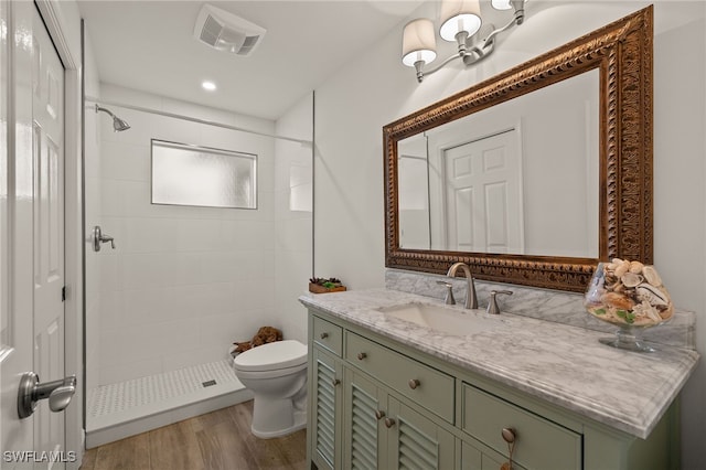 bathroom with tiled shower, hardwood / wood-style floors, vanity, and toilet