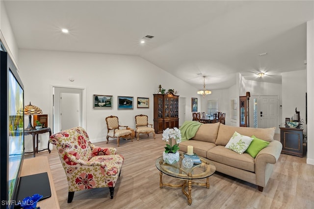 living room featuring a notable chandelier, light hardwood / wood-style flooring, and vaulted ceiling