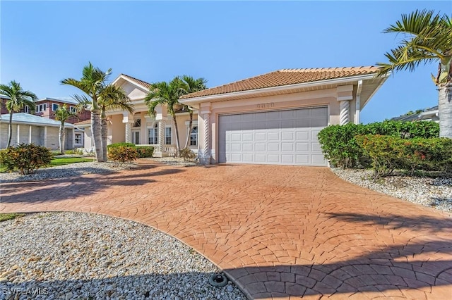 mediterranean / spanish home featuring a garage, decorative driveway, a tiled roof, and stucco siding