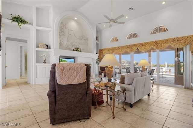 tiled living room with ceiling fan, built in shelves, and high vaulted ceiling