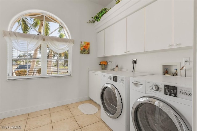 clothes washing area with cabinets, light tile patterned floors, washer and clothes dryer, and a wealth of natural light