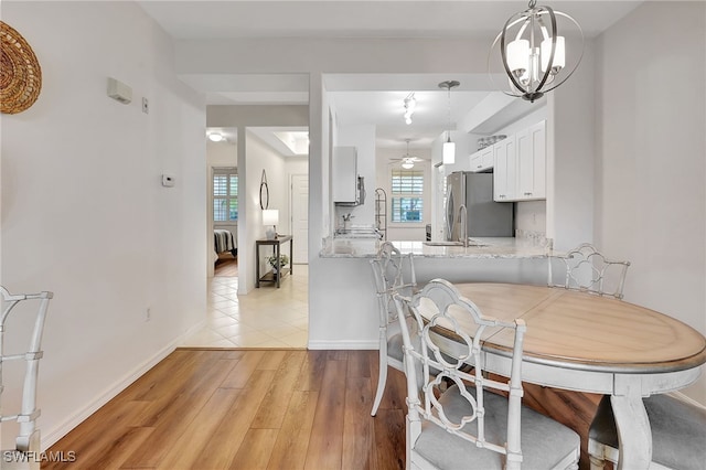 dining area featuring a wealth of natural light, sink, ceiling fan with notable chandelier, and light wood-type flooring