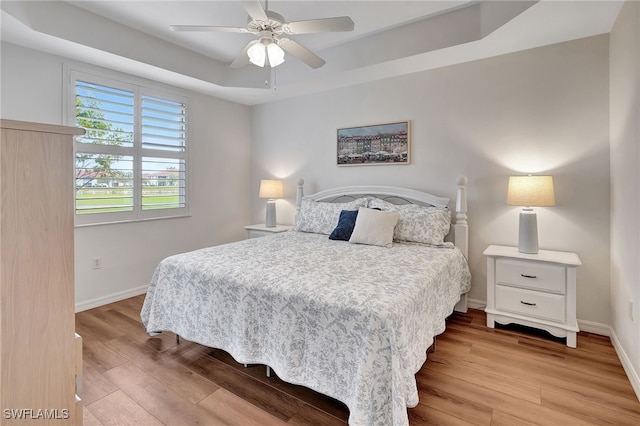 bedroom with a tray ceiling, ceiling fan, and light hardwood / wood-style floors