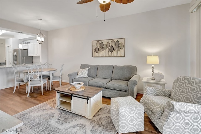 living room with ceiling fan with notable chandelier and light hardwood / wood-style floors