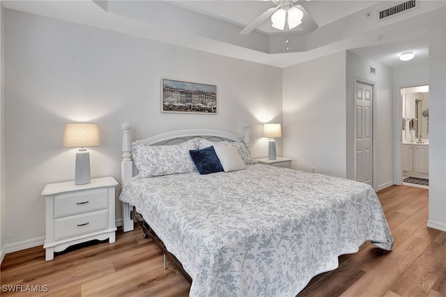 bedroom with a tray ceiling, connected bathroom, ceiling fan, and light hardwood / wood-style floors