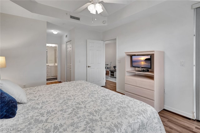 bedroom featuring wood-type flooring, connected bathroom, a raised ceiling, and ceiling fan