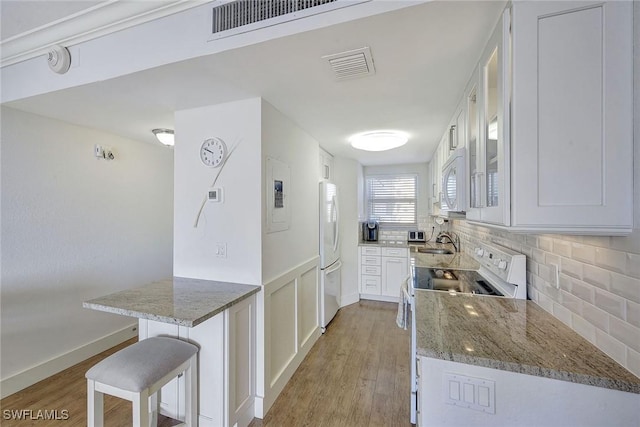 kitchen with tasteful backsplash, stone counters, a breakfast bar, white appliances, and white cabinets