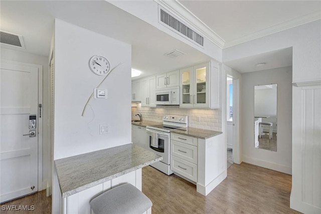 kitchen with white cabinetry, decorative backsplash, white appliances, a kitchen breakfast bar, and light stone counters