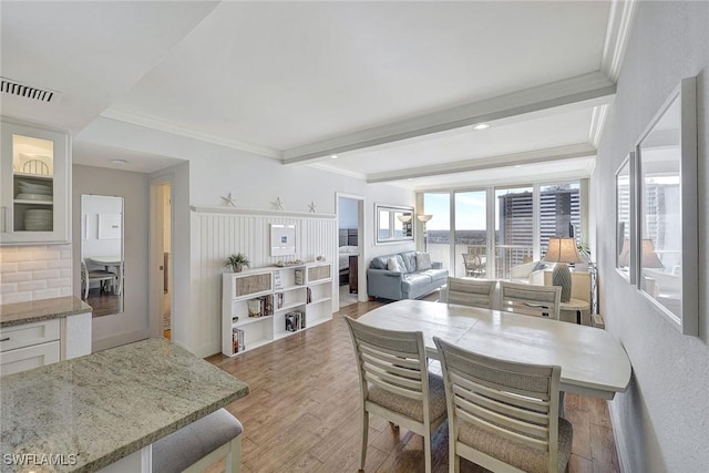 dining area with light hardwood / wood-style floors, ornamental molding, and beamed ceiling