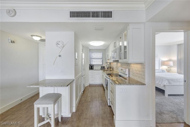 kitchen featuring a breakfast bar, kitchen peninsula, decorative backsplash, white appliances, and white cabinetry