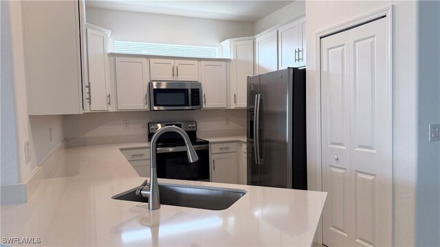 kitchen with kitchen peninsula, white cabinetry, sink, and appliances with stainless steel finishes