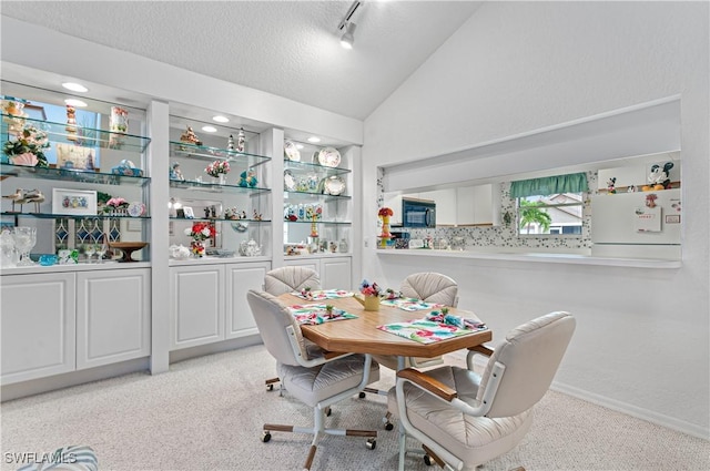 dining space featuring a textured ceiling, light colored carpet, and lofted ceiling