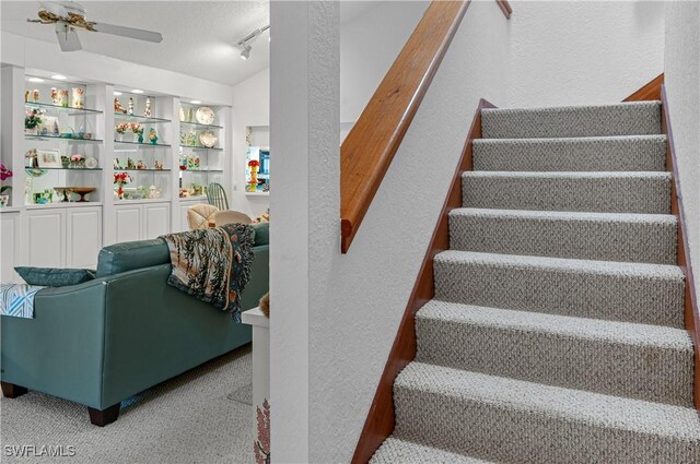 stairs with carpet, ceiling fan, and rail lighting