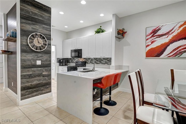 kitchen featuring black appliances, a breakfast bar, kitchen peninsula, light tile patterned flooring, and white cabinetry