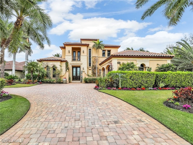 mediterranean / spanish home with a front lawn, french doors, and a balcony