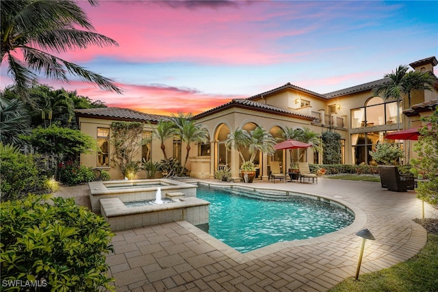 pool at dusk with a patio and an in ground hot tub