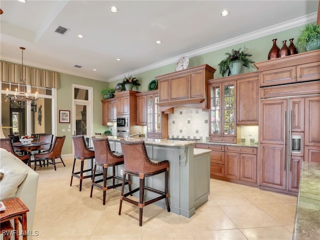 kitchen featuring a breakfast bar, hanging light fixtures, a center island, light stone counters, and built in appliances