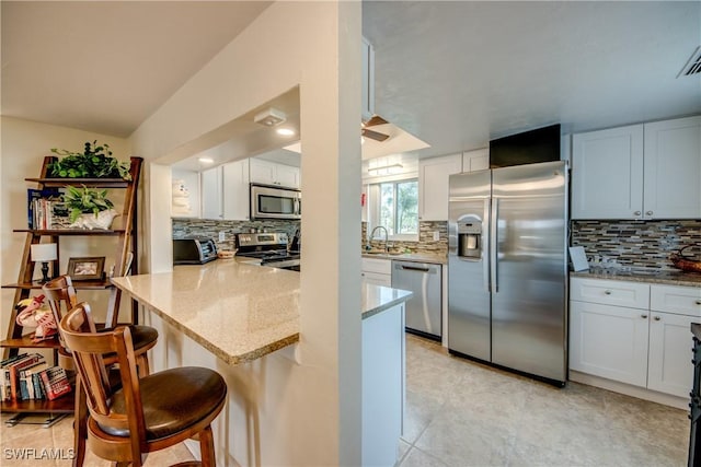 kitchen with sink, a breakfast bar area, appliances with stainless steel finishes, light stone countertops, and white cabinets