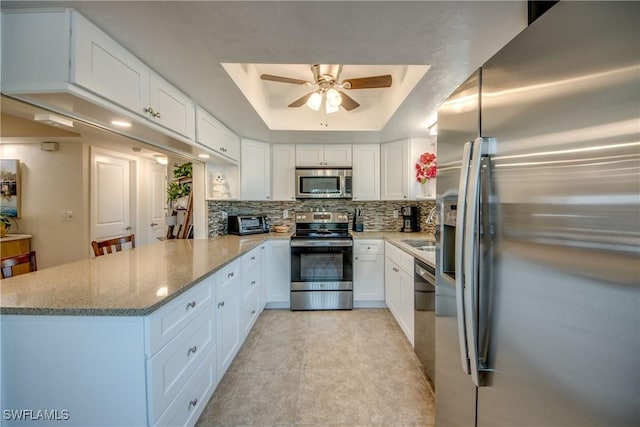 kitchen with kitchen peninsula, appliances with stainless steel finishes, backsplash, white cabinetry, and a tray ceiling