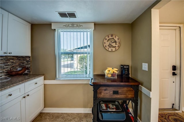 interior space featuring white cabinets, decorative backsplash, and dark stone countertops