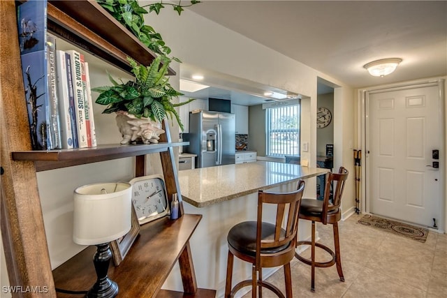 kitchen with stainless steel fridge with ice dispenser, a kitchen bar, and light stone countertops