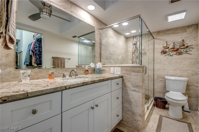 bathroom with an enclosed shower, vanity, tile walls, toilet, and ceiling fan