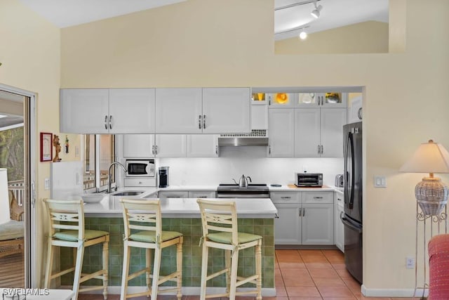 kitchen featuring black refrigerator, white cabinetry, white microwave, a breakfast bar, and vaulted ceiling