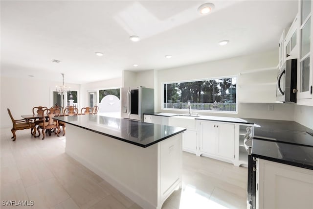 kitchen featuring appliances with stainless steel finishes, decorative light fixtures, a notable chandelier, white cabinets, and a kitchen island