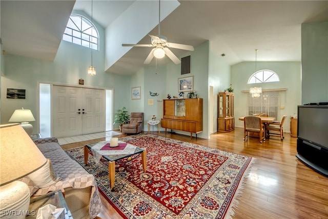 living room featuring ceiling fan with notable chandelier, high vaulted ceiling, and light hardwood / wood-style flooring