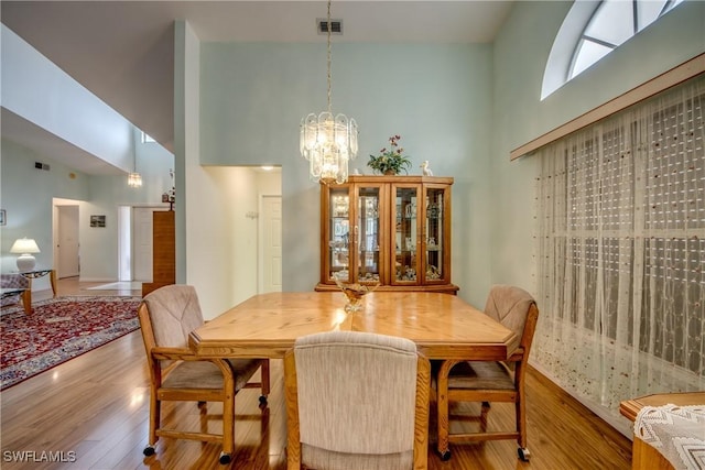 dining room featuring a towering ceiling, a chandelier, and wood-type flooring