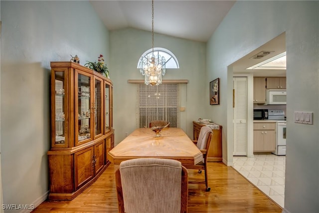 dining space with light hardwood / wood-style flooring, high vaulted ceiling, and an inviting chandelier