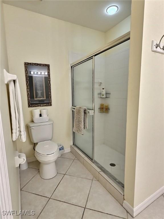 bathroom featuring toilet, a shower with shower door, and tile patterned floors