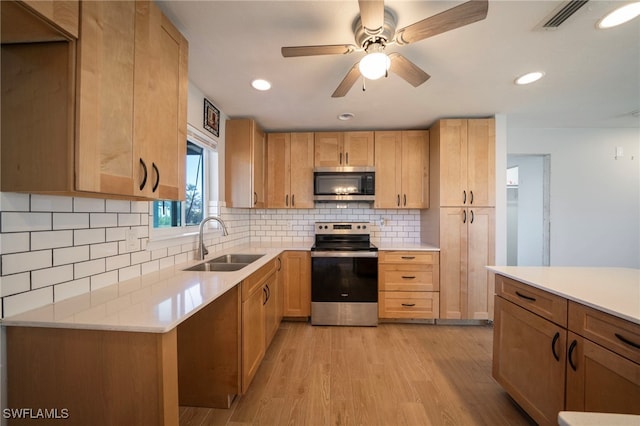 kitchen with sink, light wood-type flooring, appliances with stainless steel finishes, ceiling fan, and backsplash