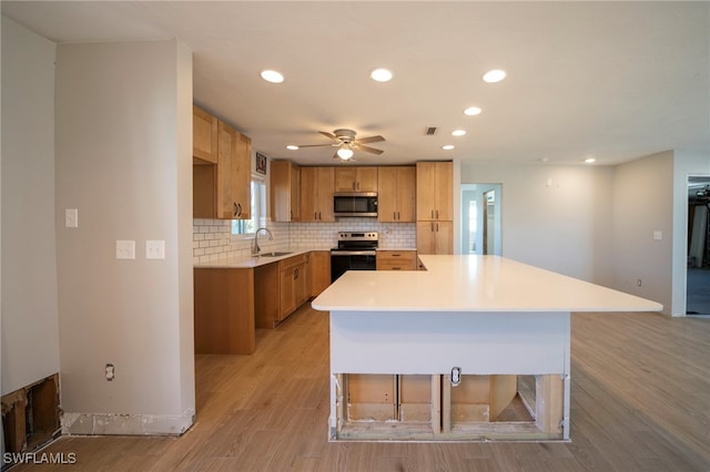 kitchen with ceiling fan, sink, a center island, backsplash, and appliances with stainless steel finishes