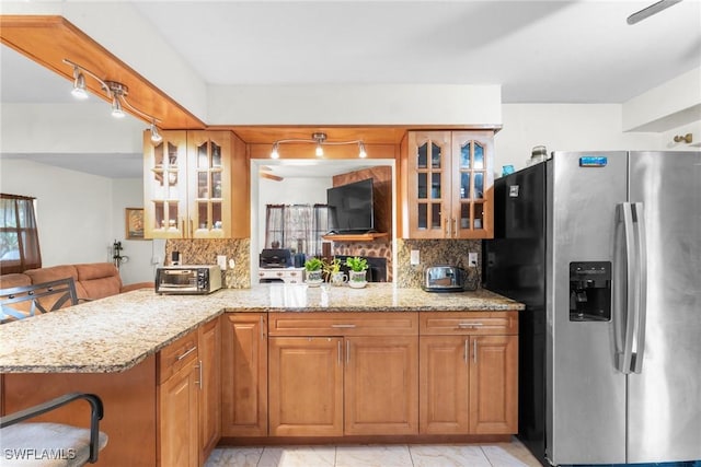 kitchen featuring light stone countertops, kitchen peninsula, stainless steel fridge, and a kitchen bar