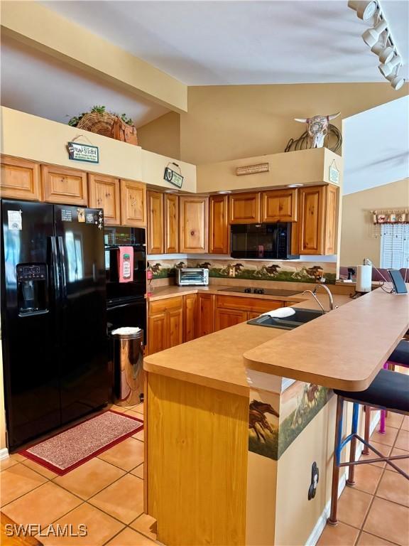 kitchen with black appliances, a breakfast bar, light tile patterned flooring, and kitchen peninsula