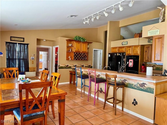 kitchen featuring black fridge, vaulted ceiling, fridge, light tile patterned flooring, and a breakfast bar area