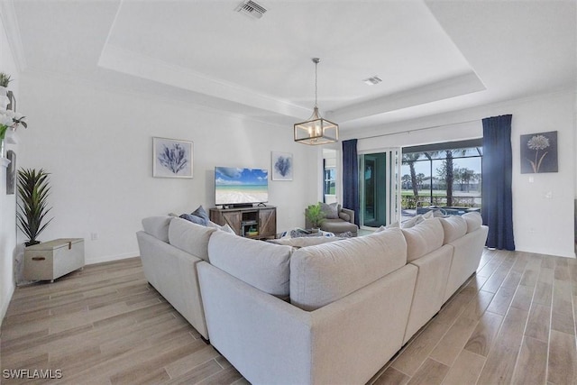 living room featuring a notable chandelier, light hardwood / wood-style floors, and a tray ceiling